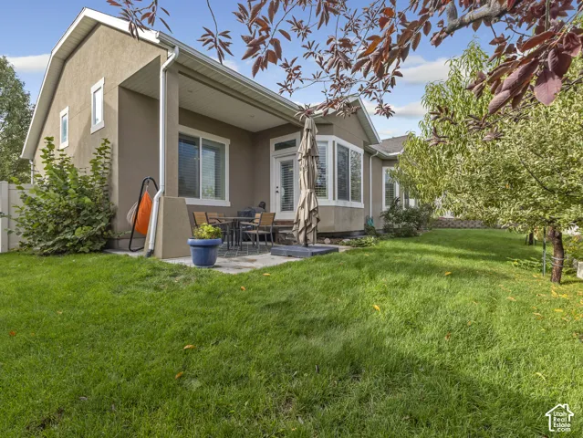 Stucco exterior featuring a covered patio, paved hardscaping, a bay window, and a manicured lawn