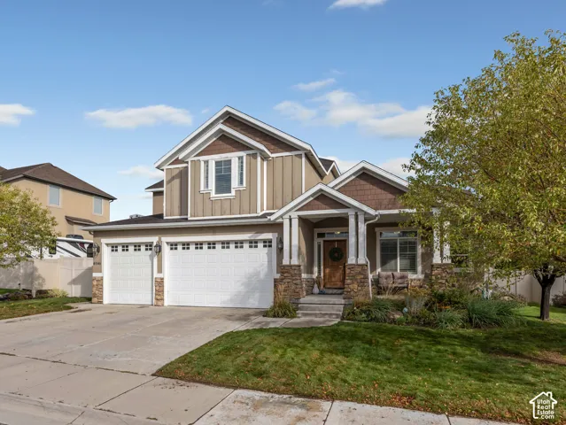 Multi-story residence featuring a board-and-batten facade with stone veneer accents, a covered front porch with column supports, and a three-car garage