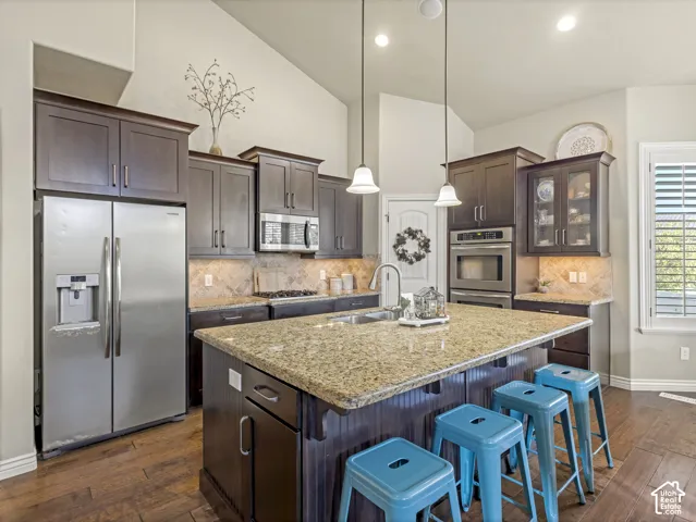 Kitchen featuring dark wood cabinetry, a central island with a stone countertop, stainless steel appliances, a tile backsplash, and wood-finish flooring