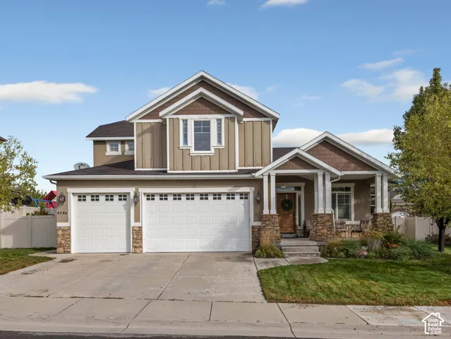 Two-story exterior featuring board-and-batten siding, stone veneer accents, multi-gabled roofline, covered front porch with square columns, and a three-car garage