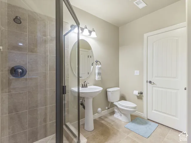 Full-bathroom featuring a tiled shower enclosure with glass door, pedestal sink, oval mirror, and multi-light vanity fixture