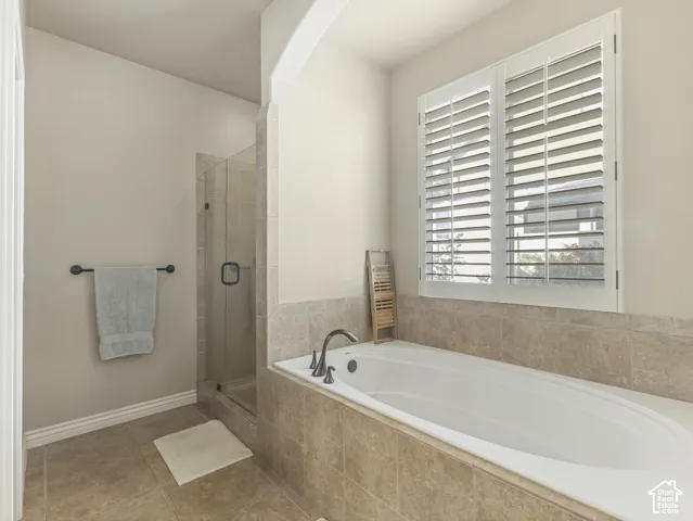Soaking tub with stone-tile surround, glass-enclosed shower, and plantation shutters