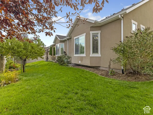 Stucco exterior featuring dual bay windows, manicured lawn, and landscape beds