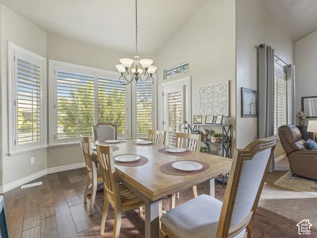 Vaulted ceilings, wood-finish flooring, bay window with plantation shutters, transom window, and multi-light chandelier