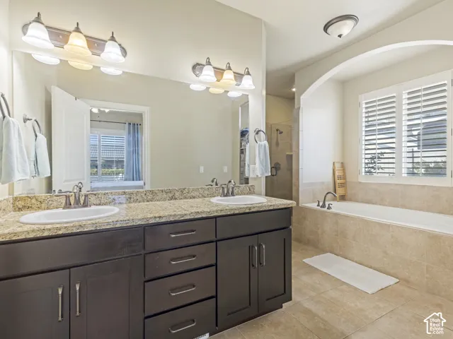 Dual-sink vanity with stone countertop, dark wood-finish cabinetry, built-in soaking tub, tile surround, and window shutters