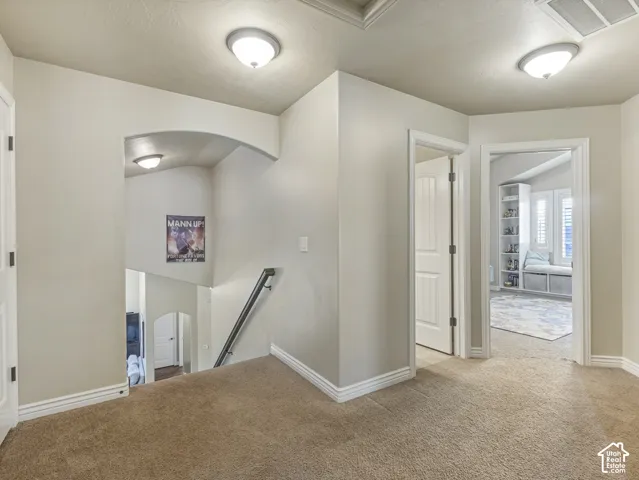 Neutral-toned interior featuring arched architectural detailing, carpeted flooring, two flush-mount ceiling light fixtures, and multi-panel interior doors