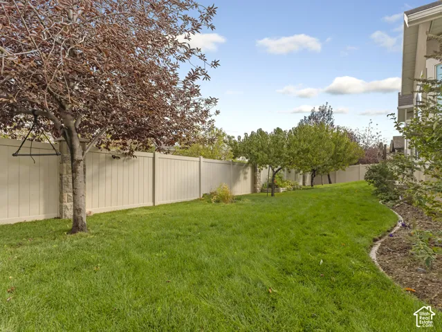 Rear yard featuring a manicured lawn, full-height vinyl perimeter fencing with stone pillars, and mature trees