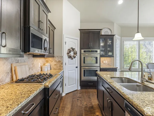 Kitchen featuring dark wood cabinetry, stone countertops, built-in double wall ovens, a gas cooktop, and wood-finish flooring