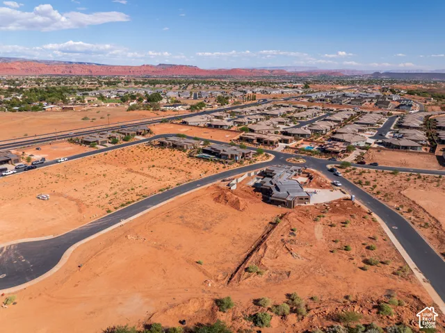 Expansive undeveloped land parcel with paved road frontage, surrounded by established residential properties and distant natural rock formations
