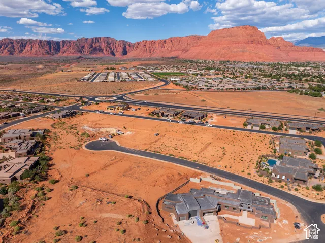 Expansive desert landscape with red rock formations, surrounded by residential developments and paved roadways