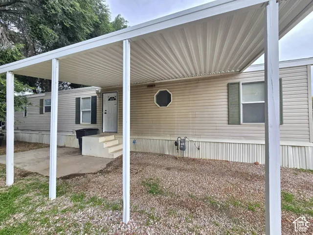 Exterior featuring horizontal vinyl siding, attached metal carport, concrete patio, octagonal accent window, and window shutters