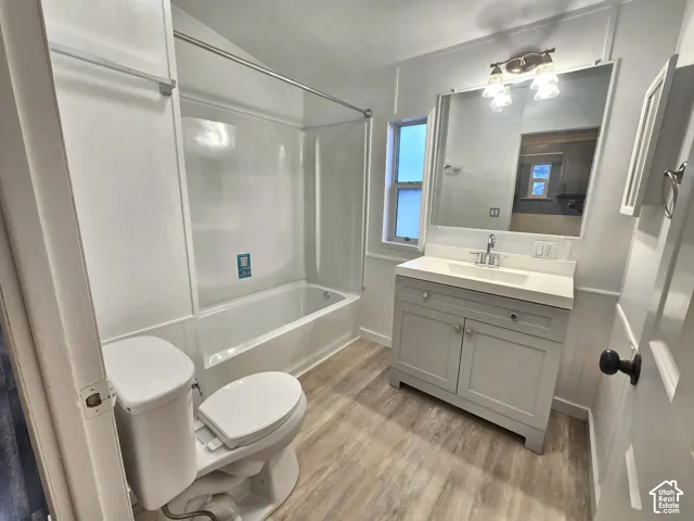 Bathroom featuring wood-finish flooring, a vanity with an integrated basin, a large wall-mounted mirror, and a tub-shower combination with surround