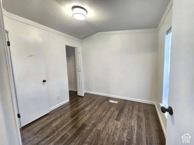 Interior room featuring wood-finish flooring, crisp white walls, crown molding, a ceiling-mounted light fixture, and a reach-in closet with a panel door