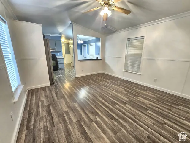 Interior space featuring wood-finish flooring, wainscoting, a ceiling fan with integrated lighting, and a pass-through opening to the kitchen