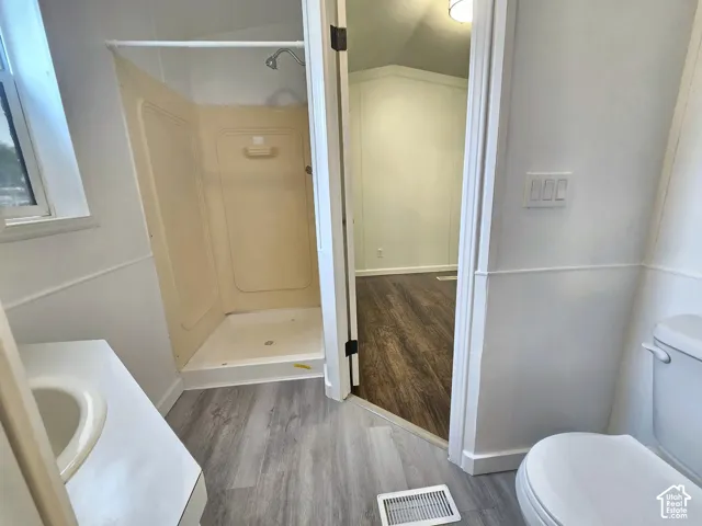 Bathroom featuring a walk-in shower with integrated surround, wood-finish flooring, and a single-basin vanity