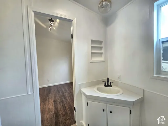 Corner vanity featuring a drop-in sink, matte black faucet, and white cabinetry, complemented by a recessed wall niche, flush-mount globe lighting, and wainscoting
