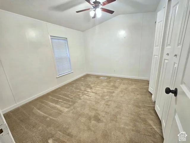 Vaulted ceiling, neutral wall-to-wall carpeting, dual-panel closet doors, and a multi-blade ceiling fan with integrated lighting