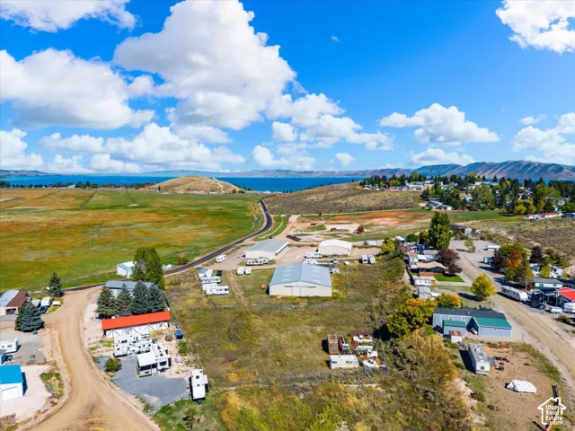 Aerial perspective of expansive acreage featuring multiple metal-sided storage structures, gravel driveways, and mountain-bordered lake scenery