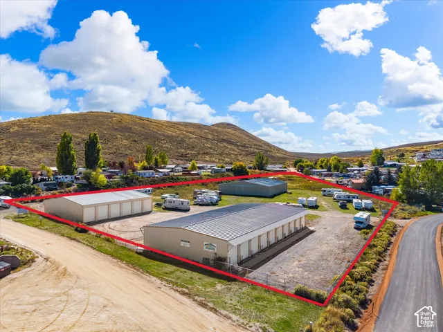 Fenced storage facility featuring multiple metal-sided structures, expansive graveled surface area, and mountain terrain backdrop