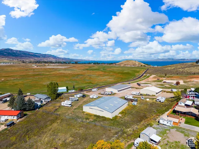 Expansive property featuring multiple large-scale metal utility buildings, extensive open acreage, and a mountain and water horizon backdrop