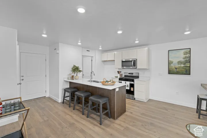 Kitchen featuring white shaker-style cabinetry, wood-finish flooring, a central island with stone-surface countertop, and stainless steel appliances