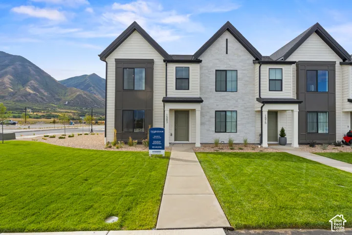 Multi-story exterior featuring a mix of horizontal siding, panel accents, and textured stone veneer, complemented by a concrete walkway and surrounding mountain backdrop