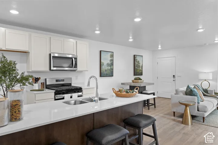 Kitchen featuring an island with a light-toned countertop and sink, dark-toned cabinetry, stainless steel appliances, and wood-finish flooring