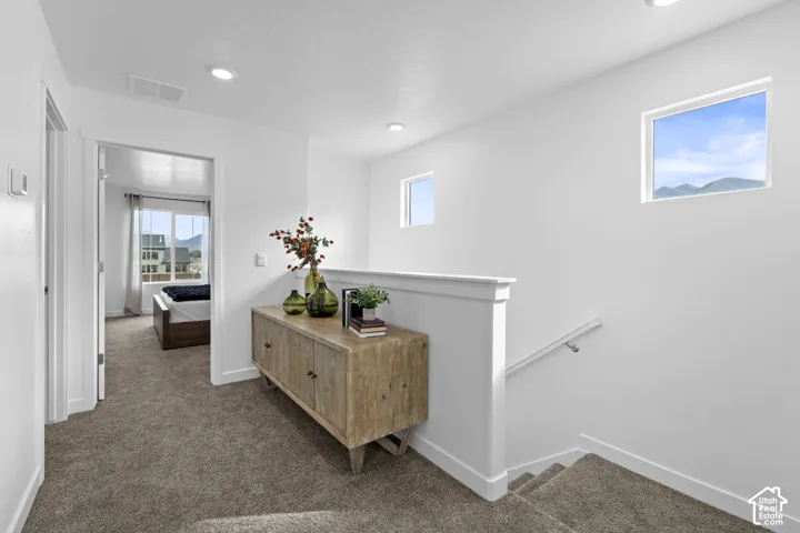 Landing area featuring carpeted flooring, recessed lighting, white half-wall railing, and two square windows