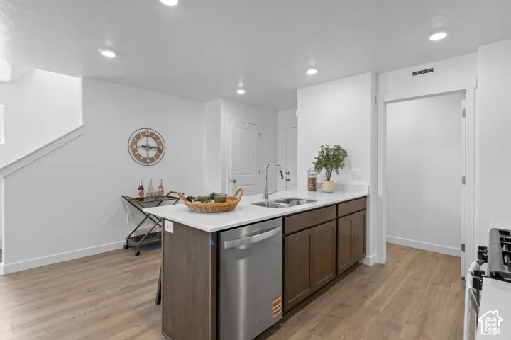 Kitchen island featuring a white stone countertop, dual-basin stainless steel sink, stainless steel dishwasher, and dark wood-finish cabinetry with recessed lighting