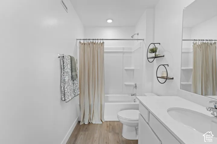 Bathroom featuring a white vanity with a light-toned countertop, integrated basin, wood-finish flooring, and a tub-shower combination with built-in shelving