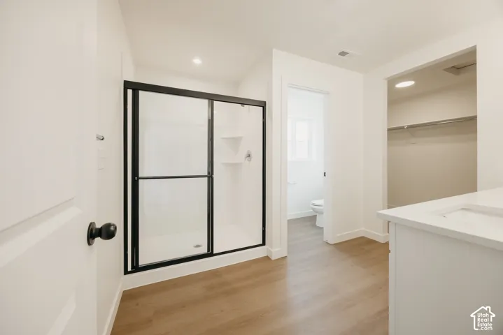Walk-in shower with a matte black frame, wood-finish flooring, white vanity with a composite countertop, and recessed lighting