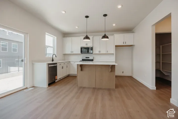 Kitchen featuring white shaker-style cabinetry, wood-finish kitchen island, stainless steel appliances, pendant lighting, and wood-finish flooring