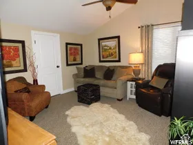 Vaulted ceiling featuring a central lighted ceiling fan, carpeted flooring, and a multi-panel interior door