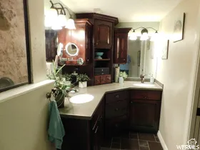 Corner vanity featuring dark wood-finish cabinetry, dual undermount sinks, solid surface countertops, and two wall-mounted light fixtures with glass shades