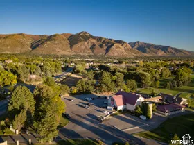 Aerial perspective featuring a property with a metal-roofed structure, paved parking area, and mature trees, set against a backdrop of mountain ranges