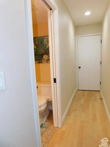 Hallway featuring light-toned wood-finish flooring, recessed ceiling lighting, and a solid-core interior door with a circular knob