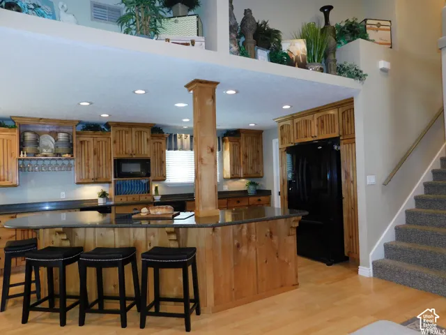 Kitchen featuring natural wood cabinetry, dark stone-finish countertops, a tiered breakfast bar, recessed lighting, and wood-finish flooring