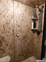 Shower enclosure featuring patterned wall surfacing, built-in corner shelving, and a dark metallic rainfall shower head with integrated hand-held sprayer