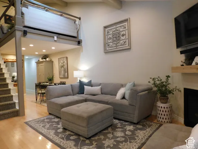 Vaulted ceilings with exposed beams, loft level featuring a cable railing, fireplace with a natural wood mantel, recessed lighting, and wood-finish flooring