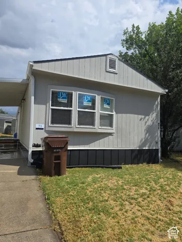 Exterior featuring light-toned vertical siding, dark base skirting, a three-pane bay window, and a concrete driveway