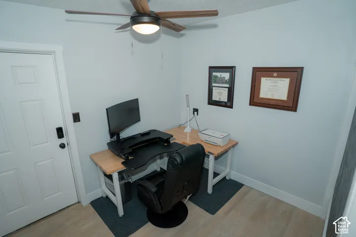 Room featuring wood-finish flooring, a multi-panel door, and a ceiling fan with integrated lighting