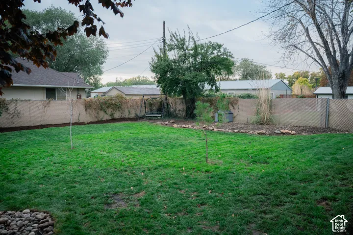Backyard featuring a grass lawn, perimeter fencing, stone ground cover, and established trees