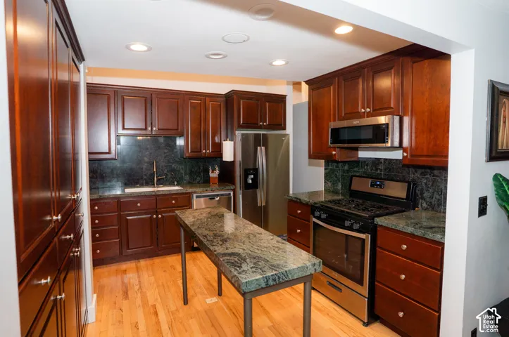 Kitchen featuring dark-toned wood cabinetry, stone countertops, stainless steel appliances, a stone tile backsplash, and wood-finish flooring