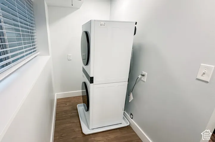 Stacked laundry unit featuring a white appliance finish, black circular door accents, and a protective floor drip tray over wood-finish flooring
