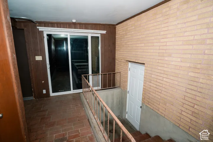 Interior space featuring brick masonry walls, terra-cotta tile flooring, sliding glass doors, and a metal staircase railing