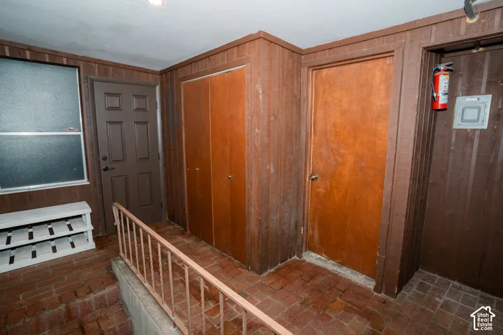 Interior space featuring vertical wood paneling, brick flooring, bi-fold wooden closet doors, a paneled solid-core door, and a metal handrail