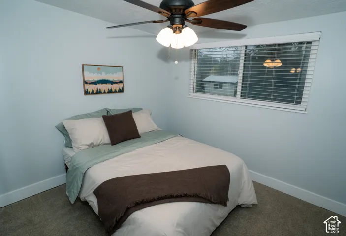 Neutral-toned carpeted flooring, multi-light ceiling fan with dark finish blades, and horizontal window blinds
