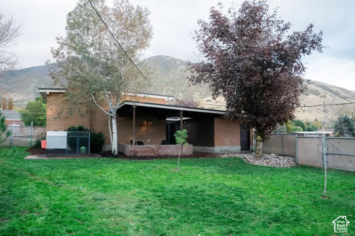 Brick exterior featuring a covered patio, expansive lawn, mature trees, and mountainous backdrop