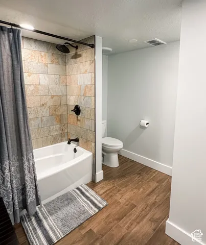 Bathroom featuring a deep soaking tub, natural stone tile shower surround, matte black plumbing fixtures, and wood-finish flooring