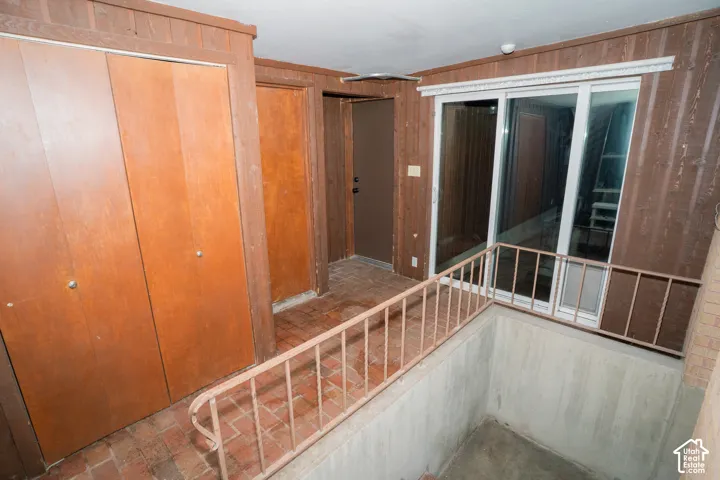 Interior space featuring wood-paneling wall finishes, tile flooring, dual-door built-in closets, and a metal stair railing